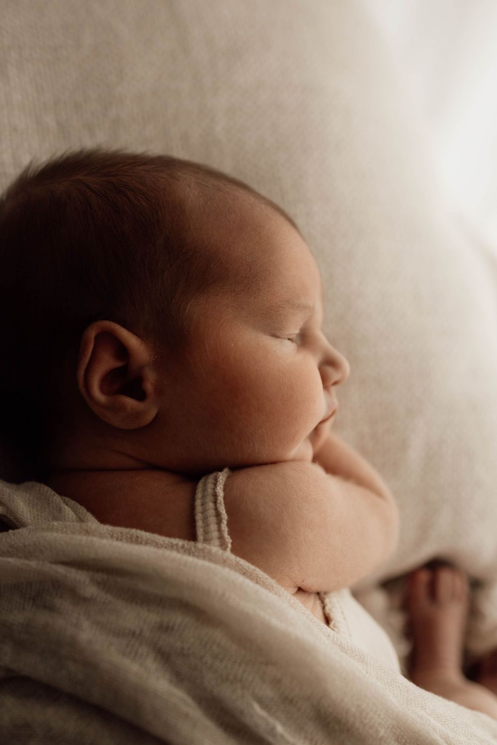 Peaceful newborn baby sleeping wrapped in a soft white blanket in warm natural light.