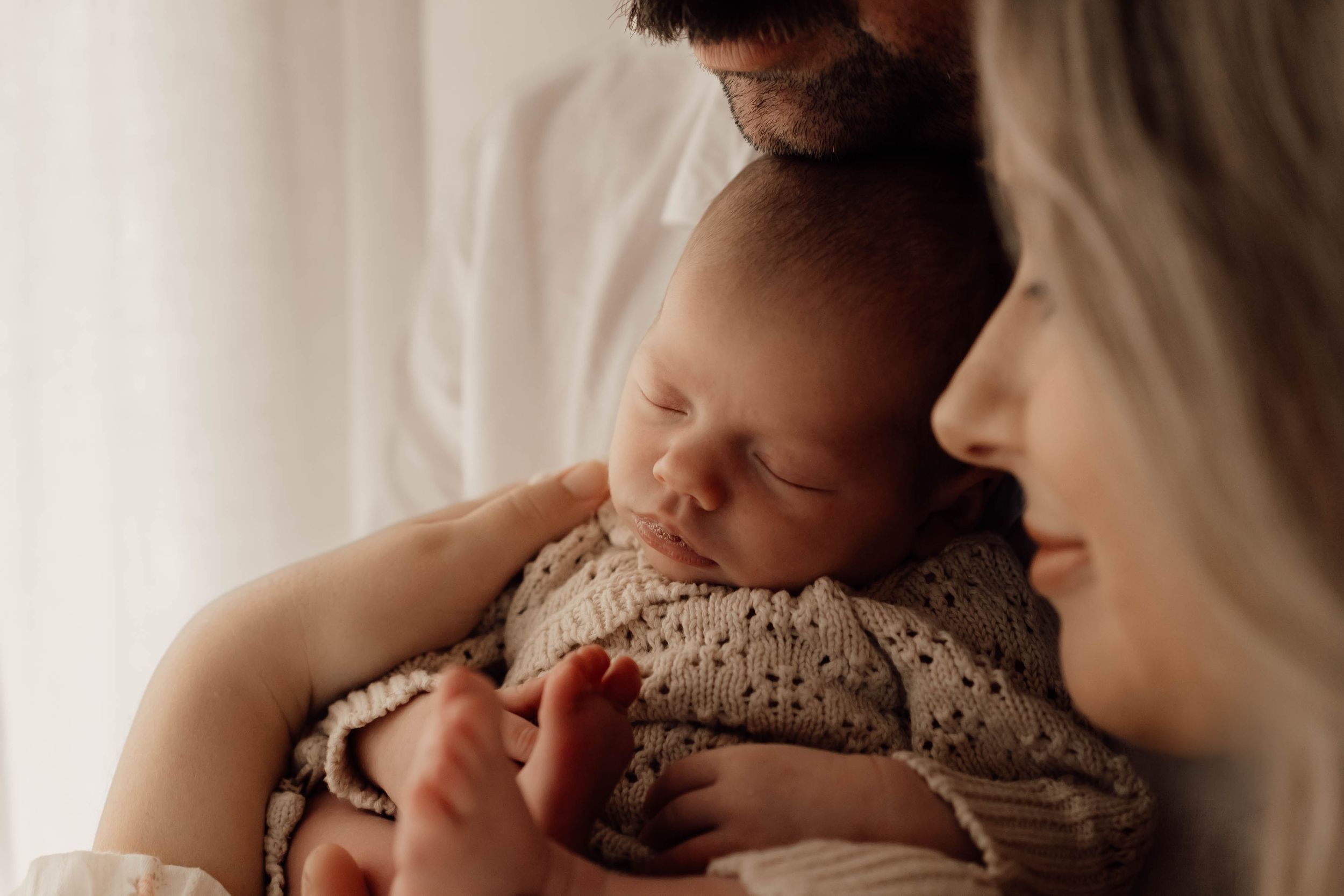 Mother and father gazing at their peacefully sleeping newborn baby wrapped in a knit outfit.