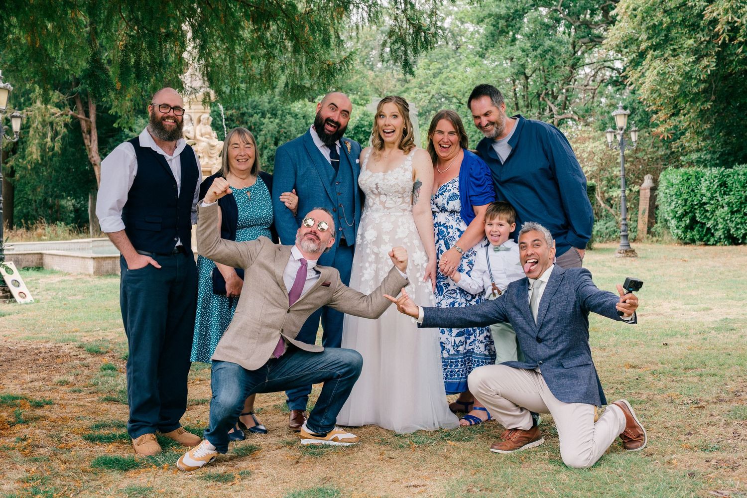 Wedding group photo with bride in white gown and guests posing joyfully outdoors in a lush green garden setting Intimate Nova Scotia wedding