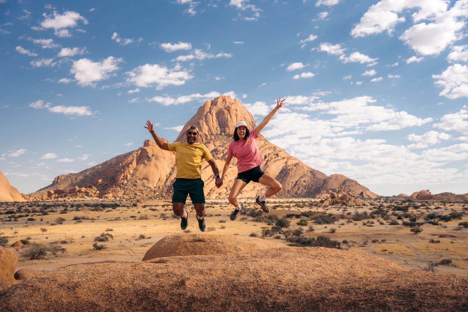 couple qui saute et lève les bras avec le smontagnes de spitzkoppe en arrière-plan