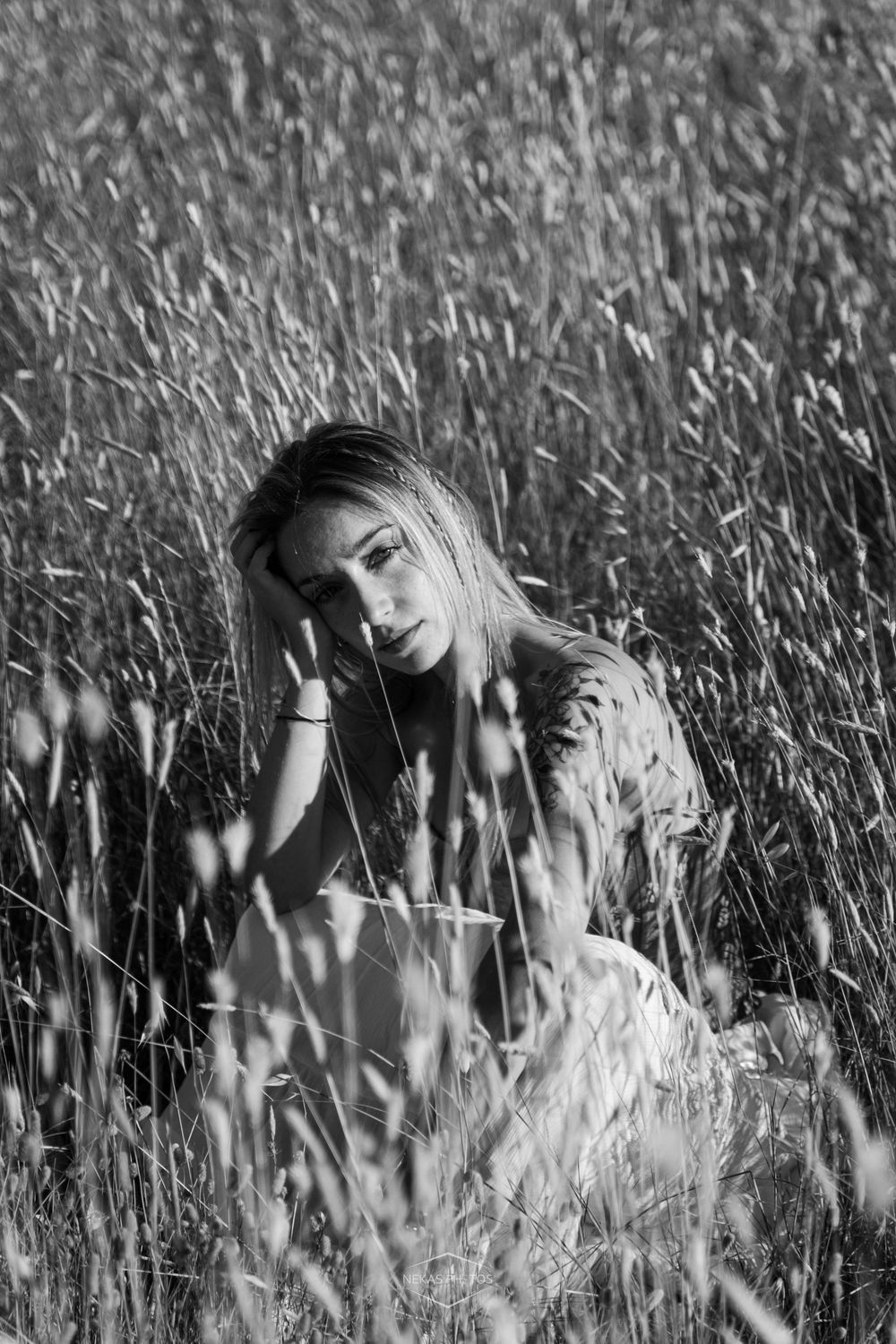 Black and white portrait of a young woman sitting peacefully in tall grass field, looking contemplative.