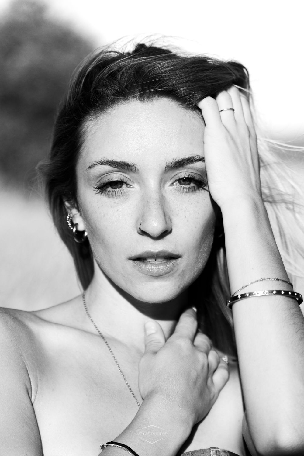 Black and white portrait of a young woman with dark hair, wearing a bracelet and necklace, posing outdoors.