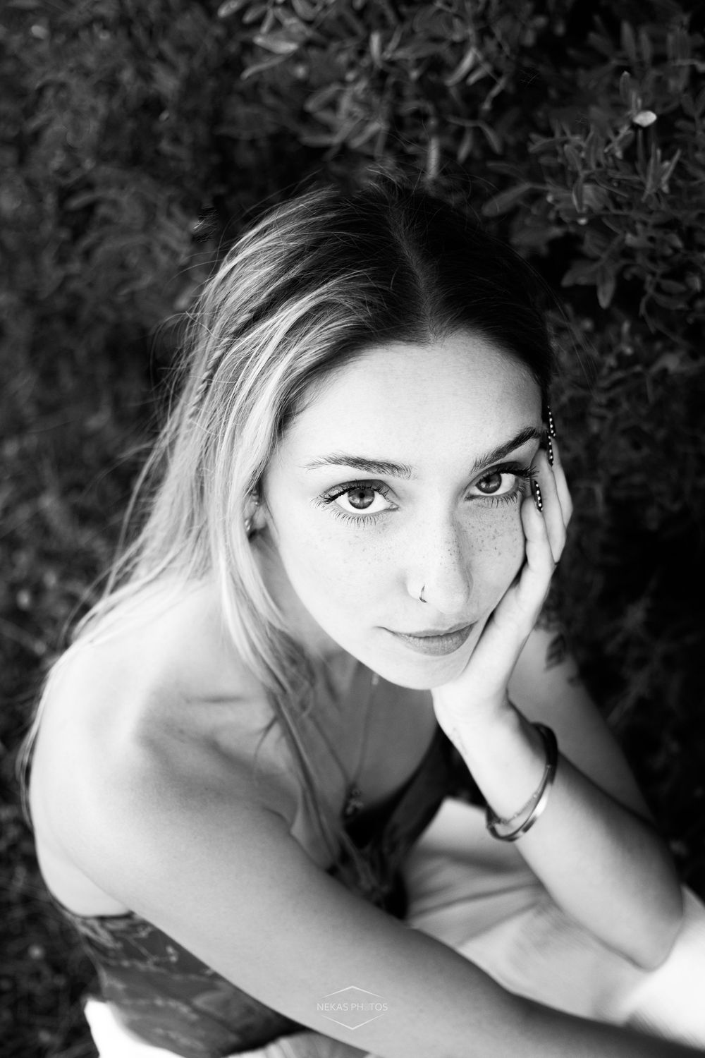 Black and white portrait of a young woman resting her cheek on her hand, looking up with a gentle gaze.