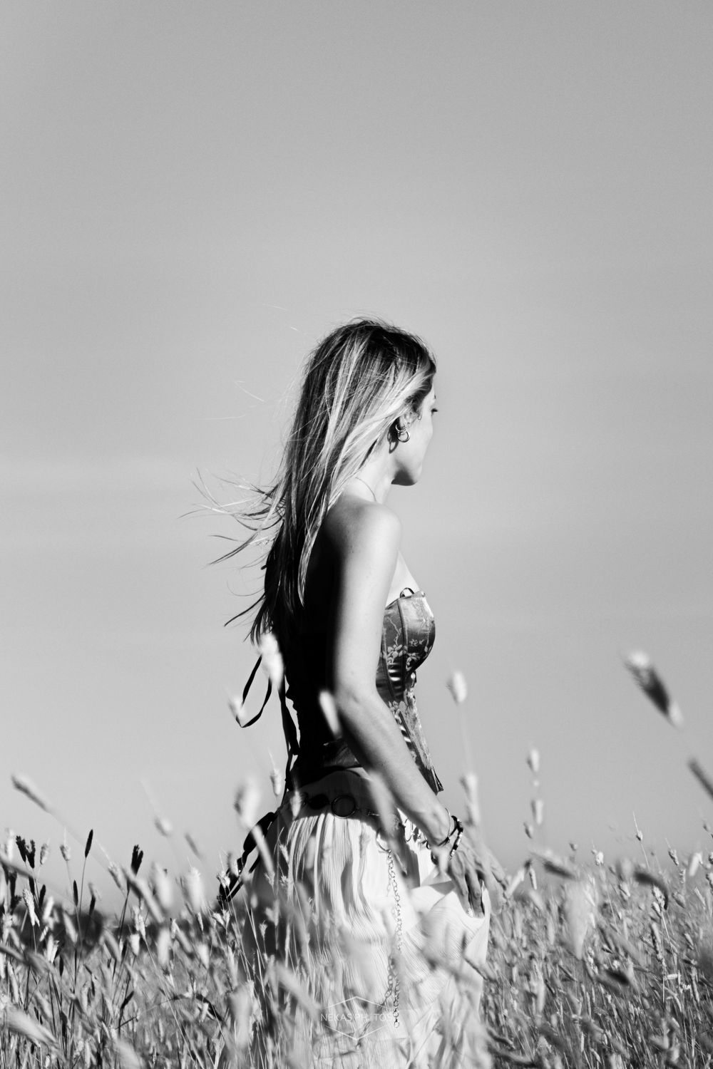 Black and white photo of a woman with flowing hair standing in a wheat field, wearing a summer dress in natural light.
