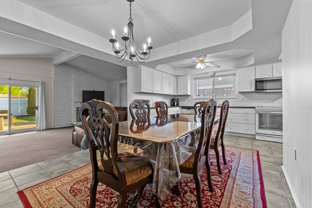 Open dining area with chandelier, dark wood table, red rug, white kitchen cabinetry, and sliding door to patio.