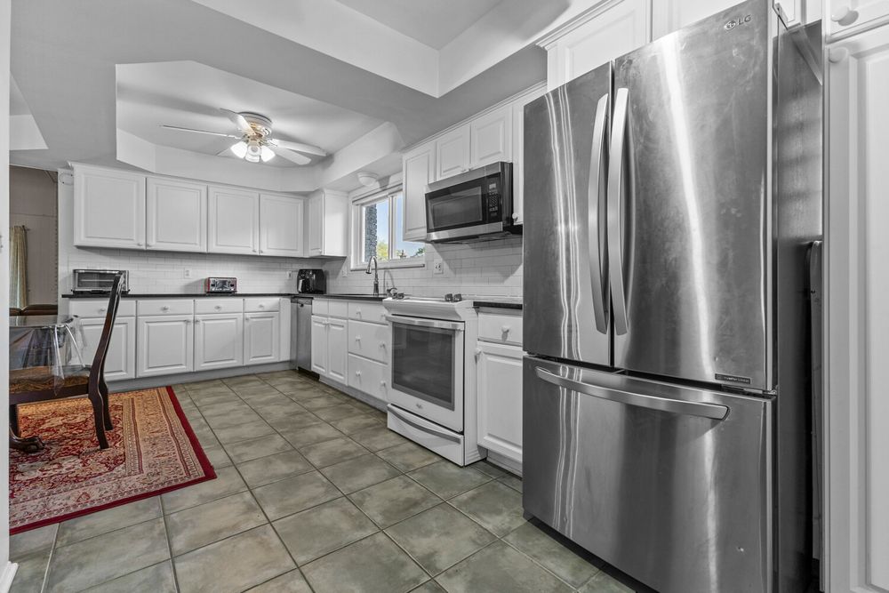 Bright white kitchen with tile floors, stainless steel refrigerator, white range, microwave, and tray ceiling.
