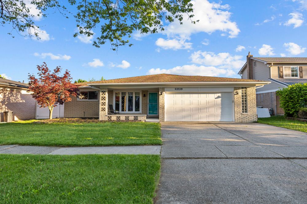 Beige brick ranch home with teal entry door, single garage, decorative lattice accents, and a lush green front yard.