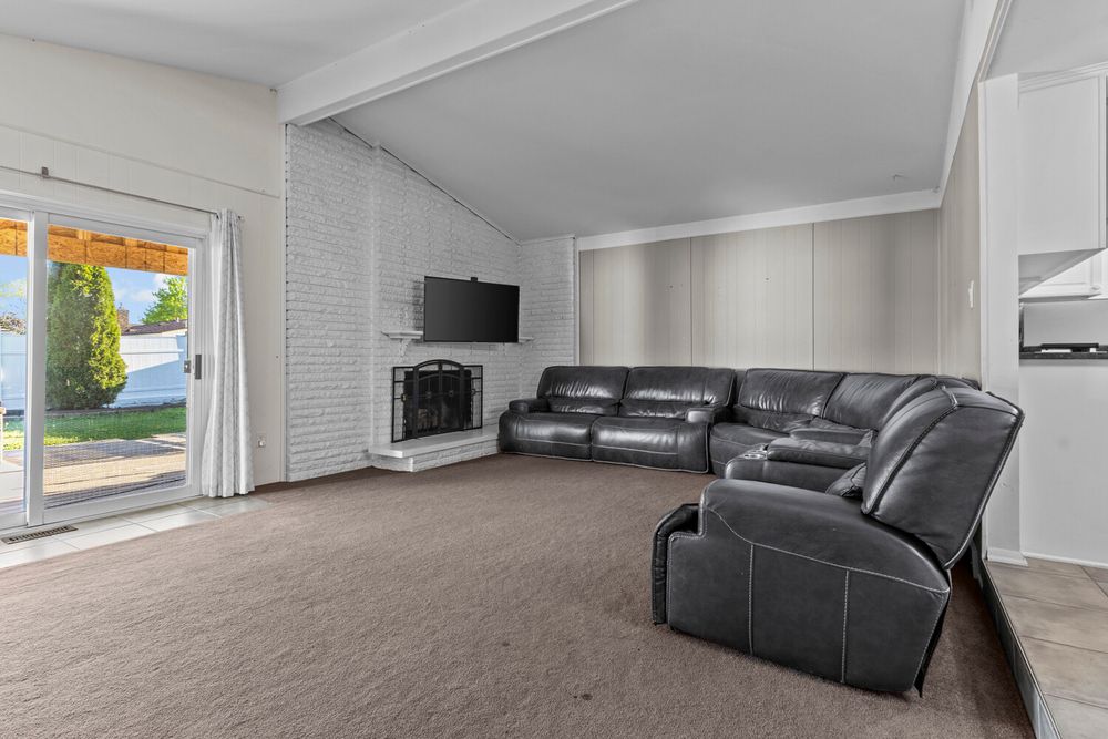 Cozy family room with vaulted beamed ceiling, brick fireplace, leather sectional sofa, and sliding door to backyard.
