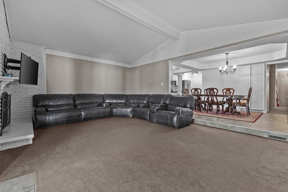 Large carpeted living room with leather sectional sofa, brick fireplace, and open view to formal dining room.