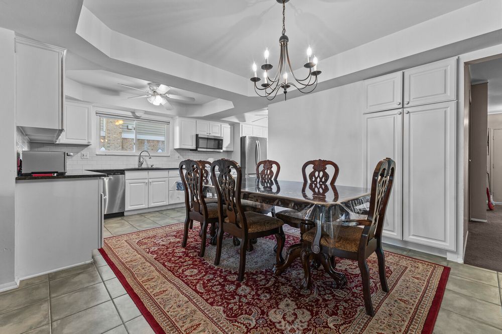 Elegant dining room with tray ceiling, chandelier, dark wood table set, red area rug, and white cabinetry.