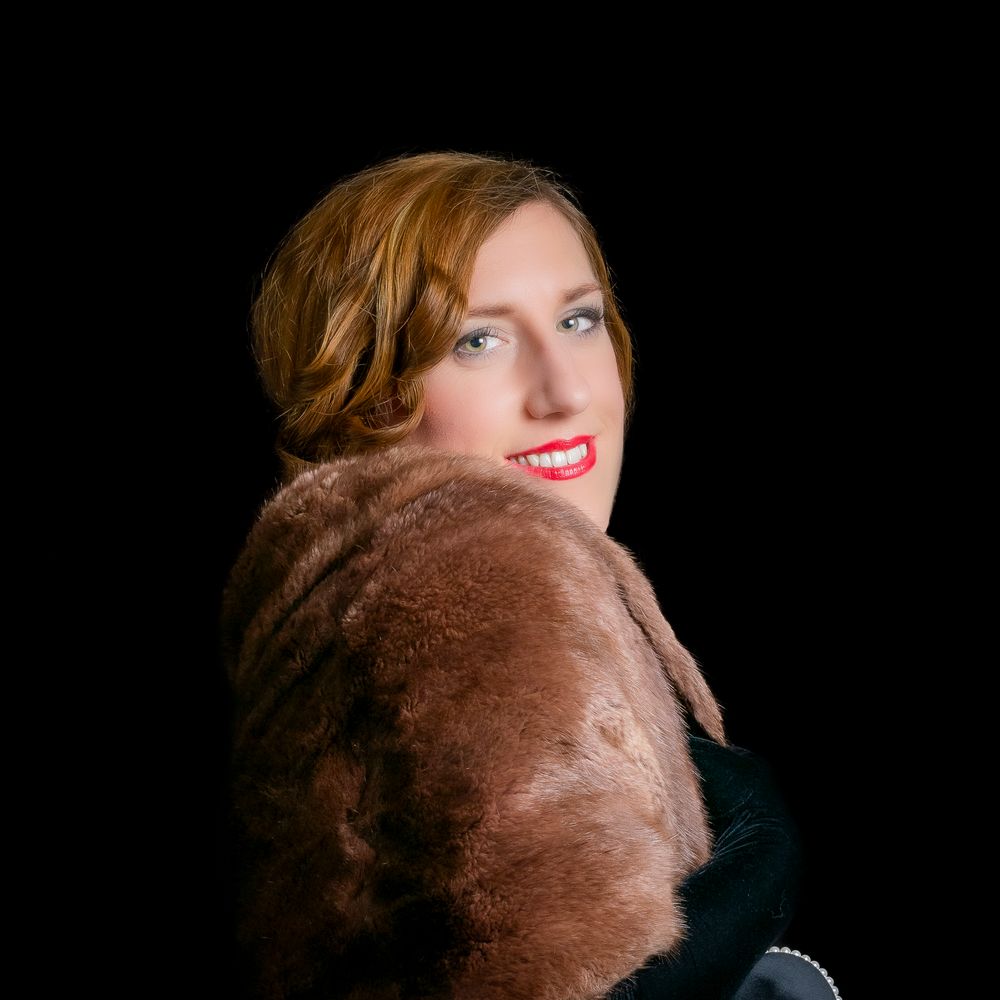 Woman in vintage fur stole poses elegantly against black background with red lips.