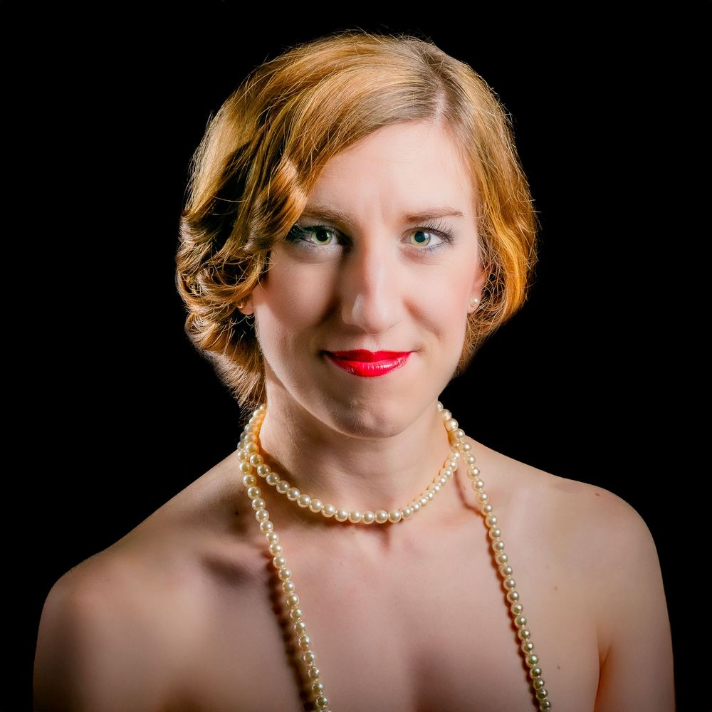 Elegant woman with red lips and pearl necklace, vintage 1920s flapper style portrait against black background.