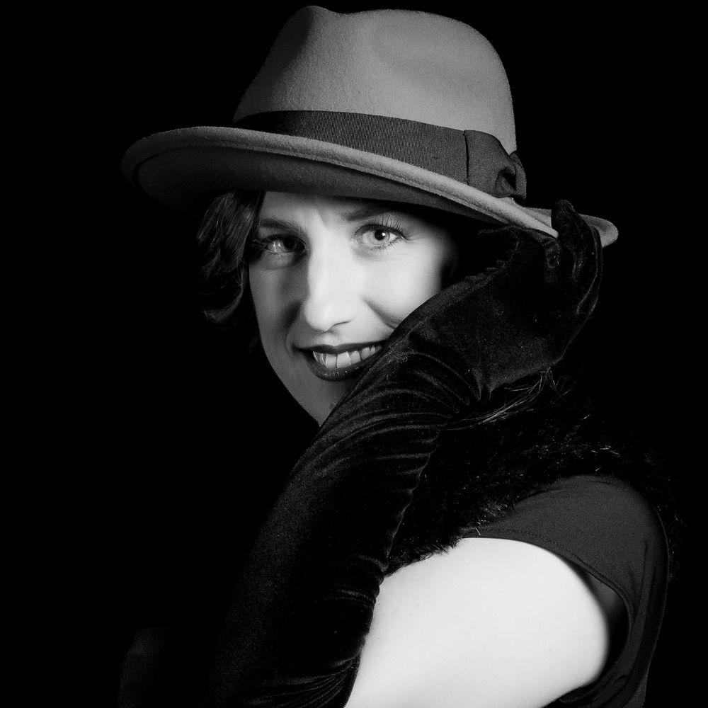 Black and white portrait of a smiling woman in a fedora hat holding a dark feather boa.