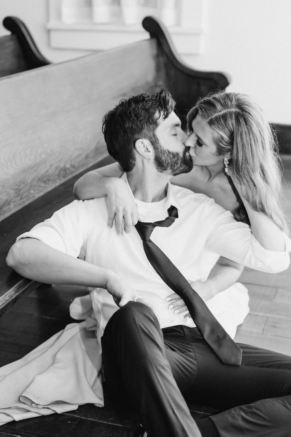 Black and white photo of a couple sharing a romantic kiss while sitting on the floor of a church.