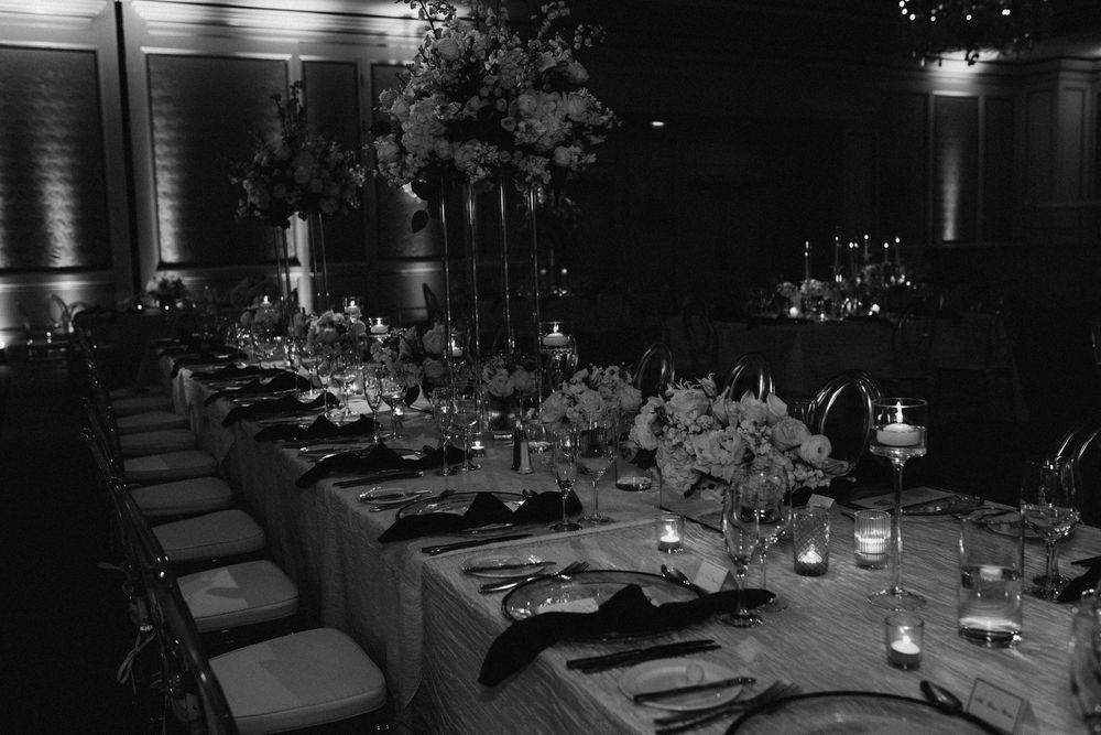 Elegant black and white photo of a long banquet table set for a formal dinner event with floral centerpieces and candles.
