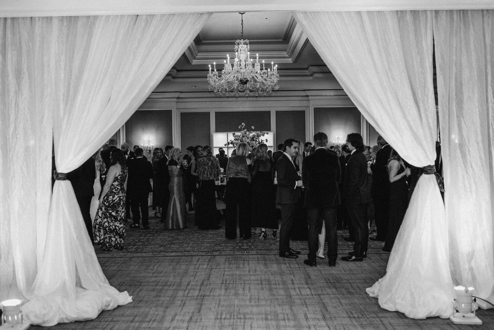 Black and white photo of elegant wedding reception ballroom entrance with draped curtains and chandelier.
