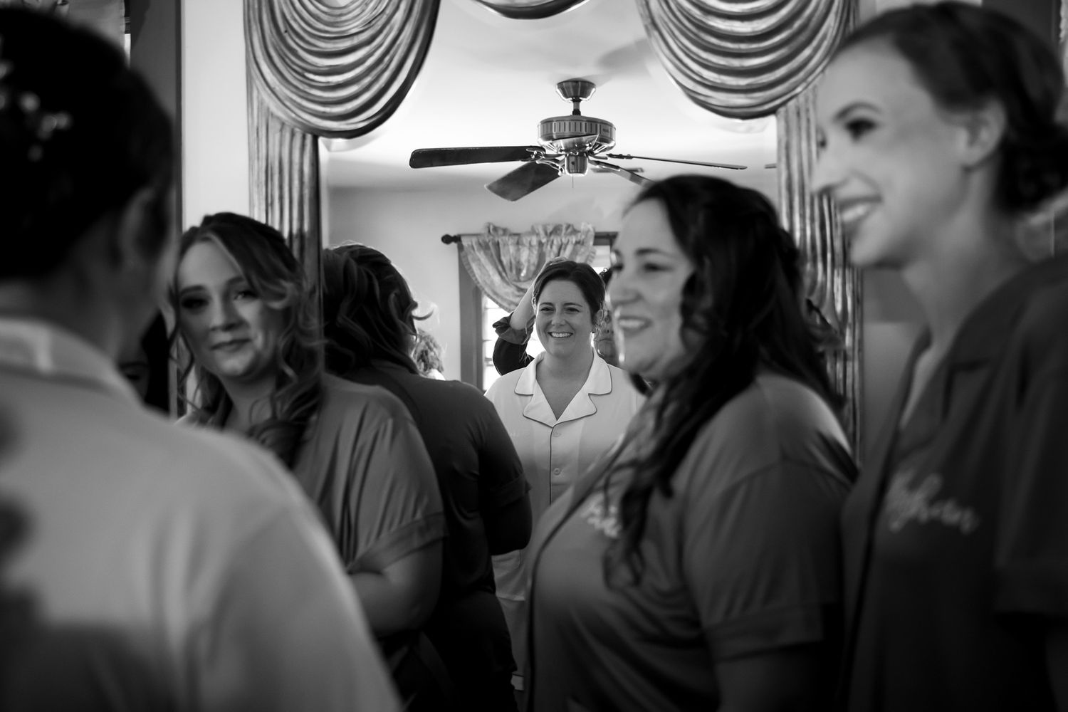 Black and white photo of bridesmaids in matching robes laughing together while getting ready for a wedding.