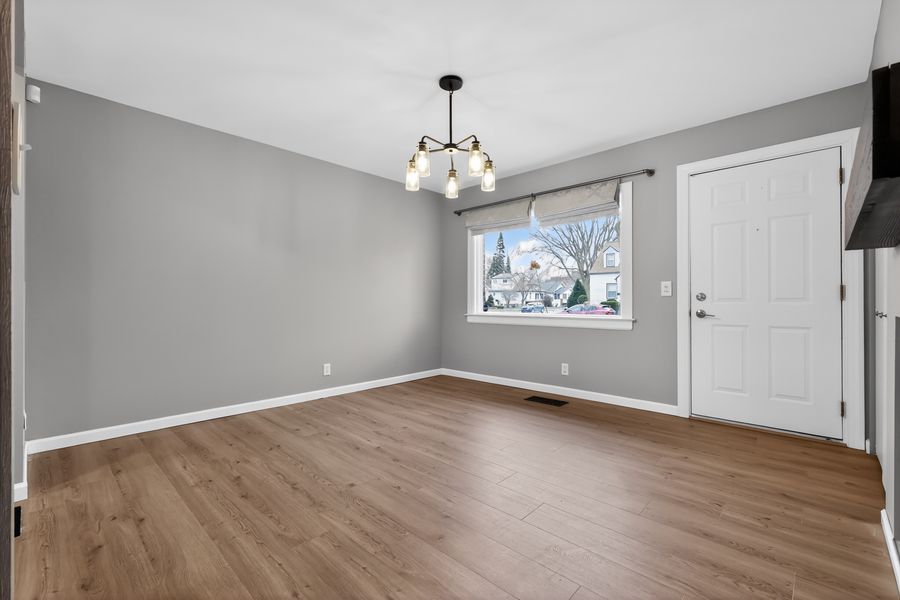 Bright dining area with hardwood floors, chandelier, large window, and neutral gray walls.