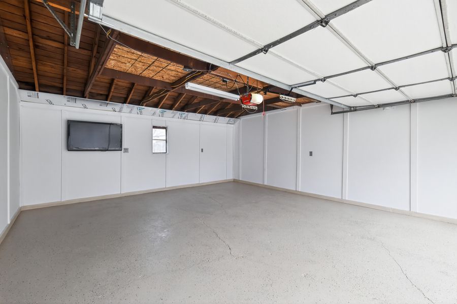 Spacious empty garage interior with white walls, concrete floor, ceiling fan, wall-mounted TV, and open garage door.