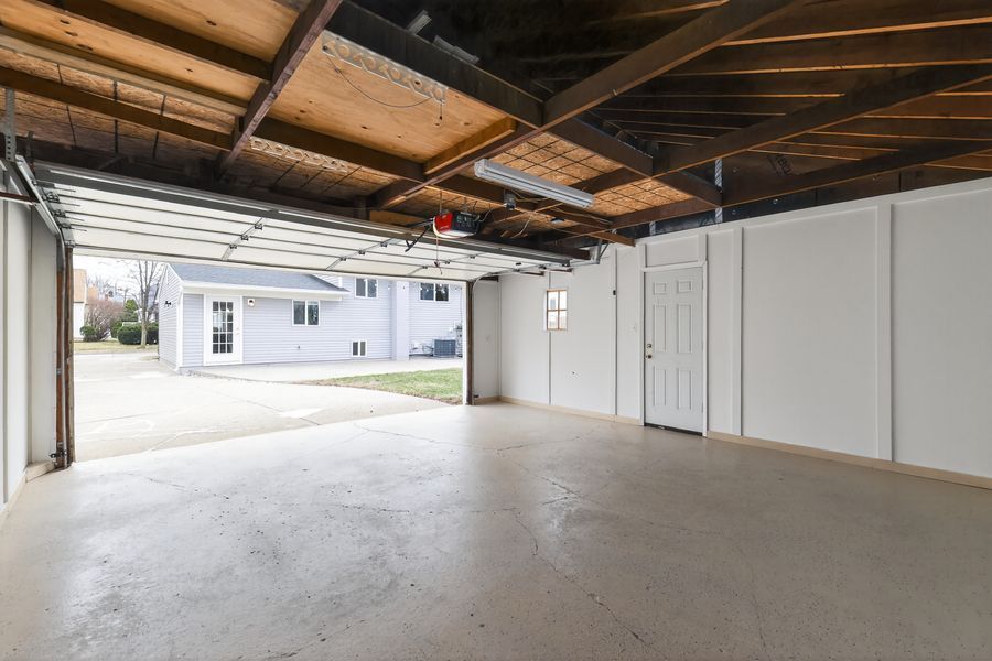 Spacious two-car garage with concrete floor, open door revealing driveway and neighboring home.