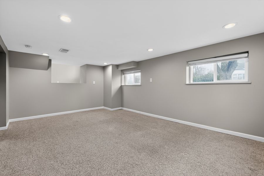 Spacious basement room with gray walls, neutral carpet, recessed lighting, and two small windows.