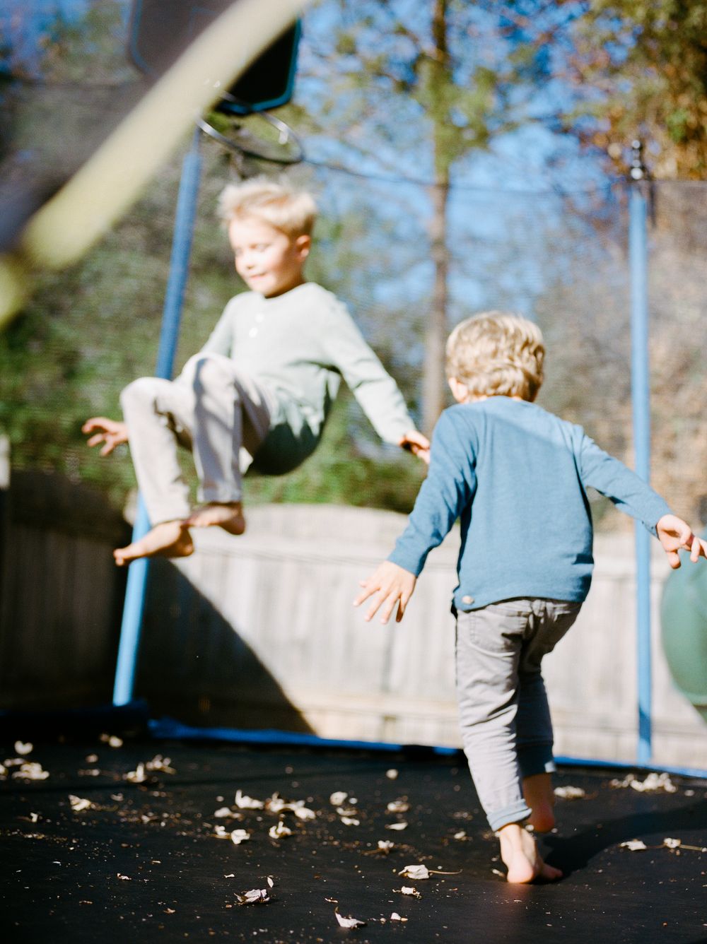 Two blonde children playing on a trampoline outdoors on a sunny day.