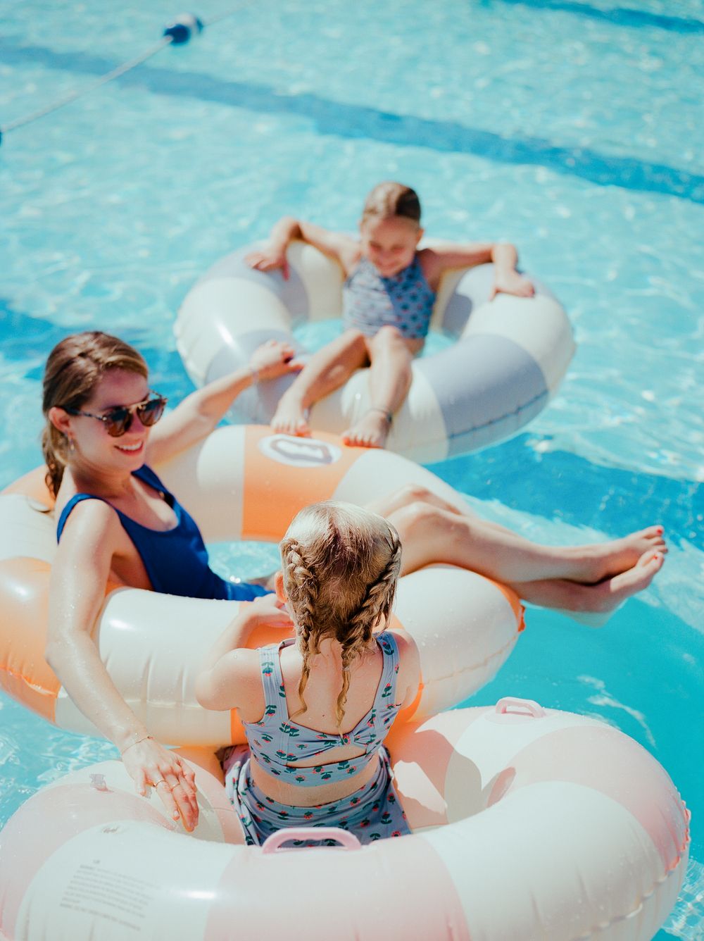 Family enjoying a sunny day floating in inflatable rings in a outdoor swimming pool.