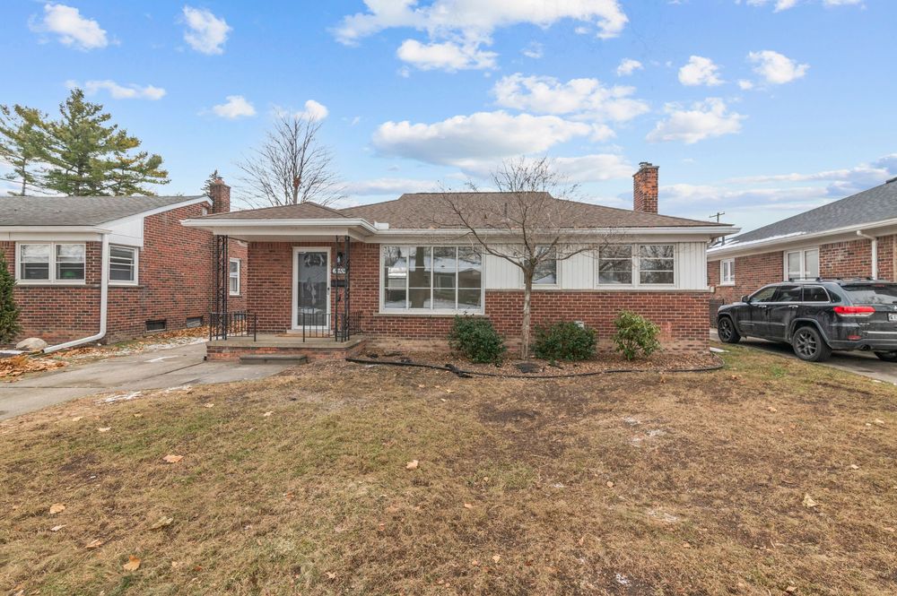 Brick ranch-style home with large front yard, bay window, and driveway with parked SUV on a clear day.