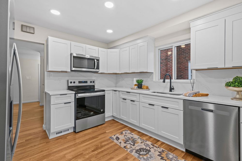 Modern white kitchen with stainless steel appliances, shaker cabinets, subway tile backsplash, and hardwood floors.