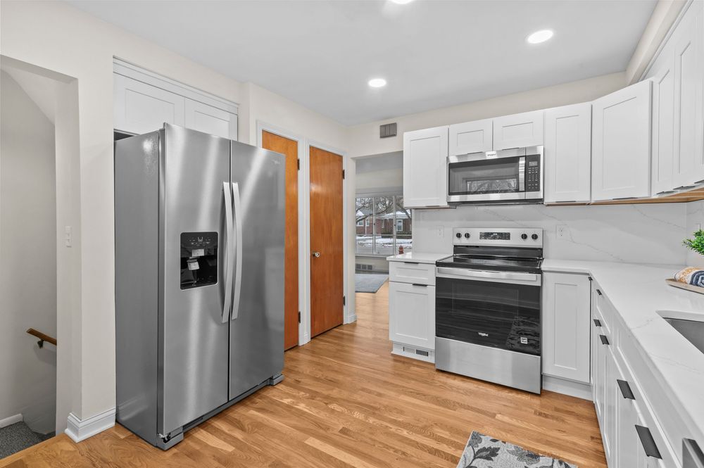 Modern kitchen with stainless steel appliances, white cabinets, and light hardwood floors.