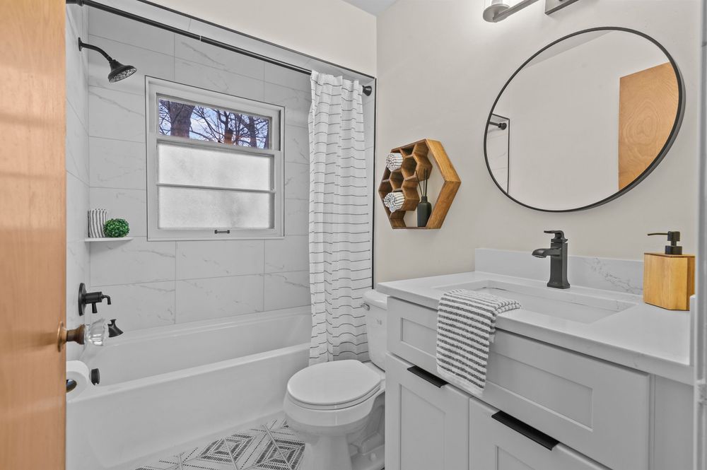 Modern bathroom with white vanity, round mirror, tiled shower-tub combo, and marble floor tiles.