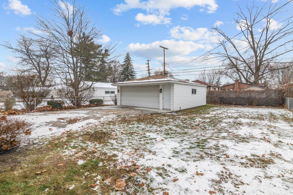 Snow-dusted backyard with white detached garage, bare trees, and wooden fence in a suburban winter setting.