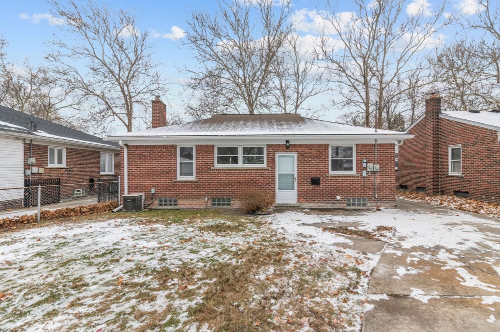 Brick ranch home with snowy front yard, bare trees, and a concrete driveway on a winter day.