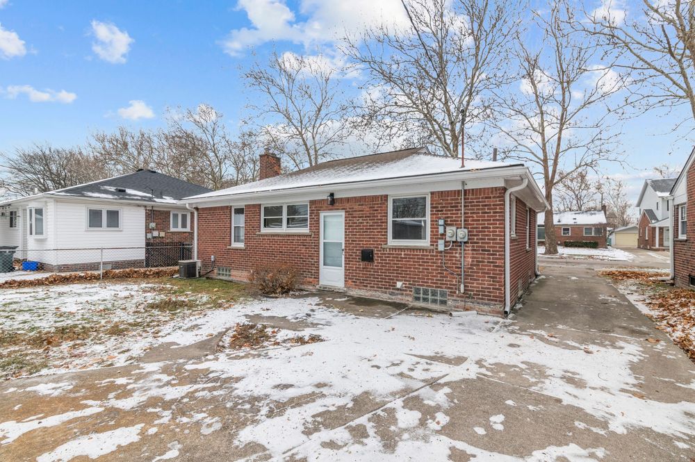 Brick ranch home with snow-dusted yard, chimney, and driveway on a winter day with bare trees in background.