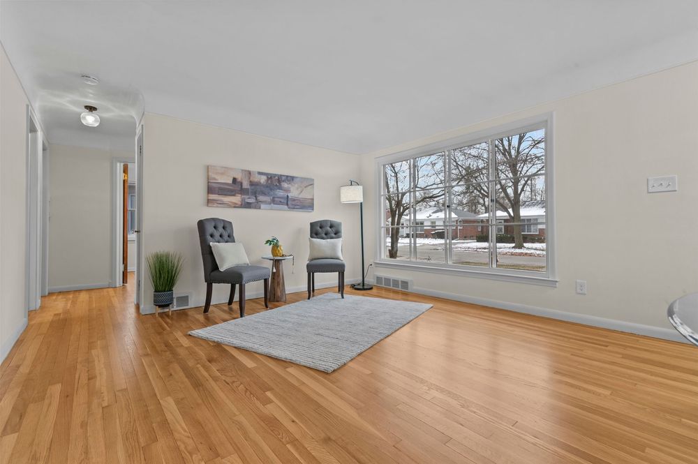 Bright living room with hardwood floors, two gray chairs, a small rug, and a large window with natural light.