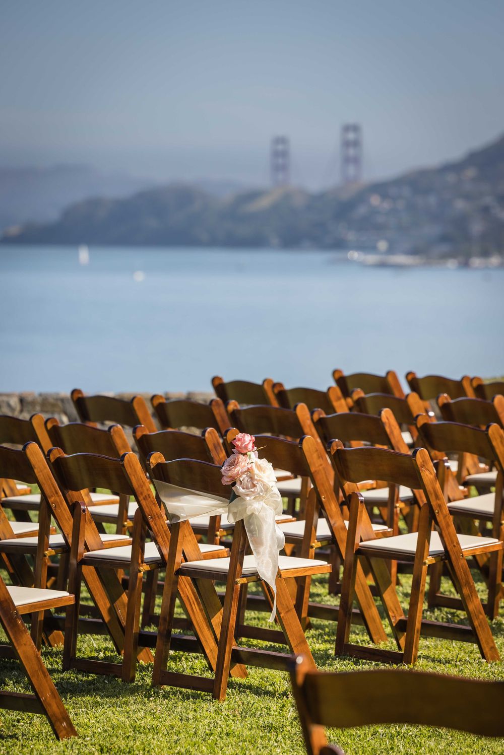 Outdoor wedding ceremony chairs arranged on green lawn with Golden Gate Bridge visible across the bay.