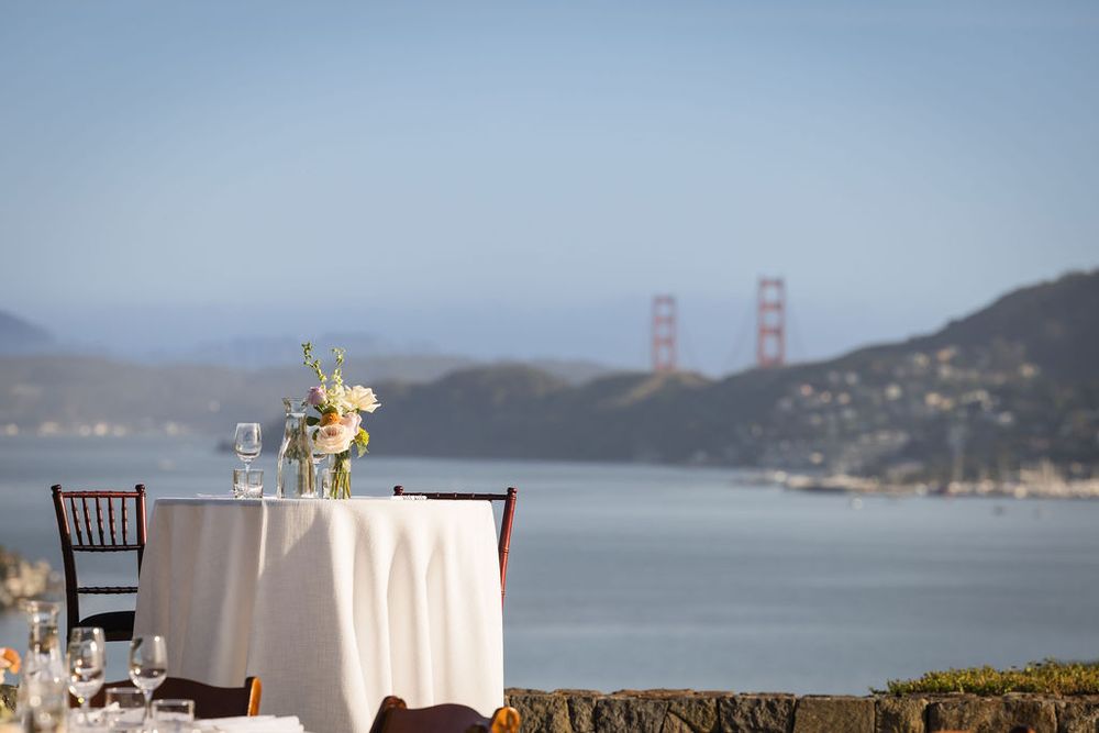 Elegant outdoor dining table with white tablecloth and floral centerpiece overlooking the Golden Gate Bridge in San Francisco.