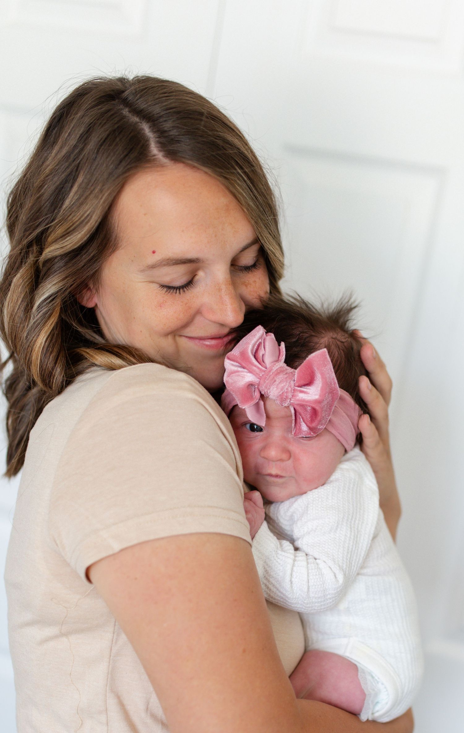 Mom gently kissing her newborn baby's head in a beautifully lit master bedroom
