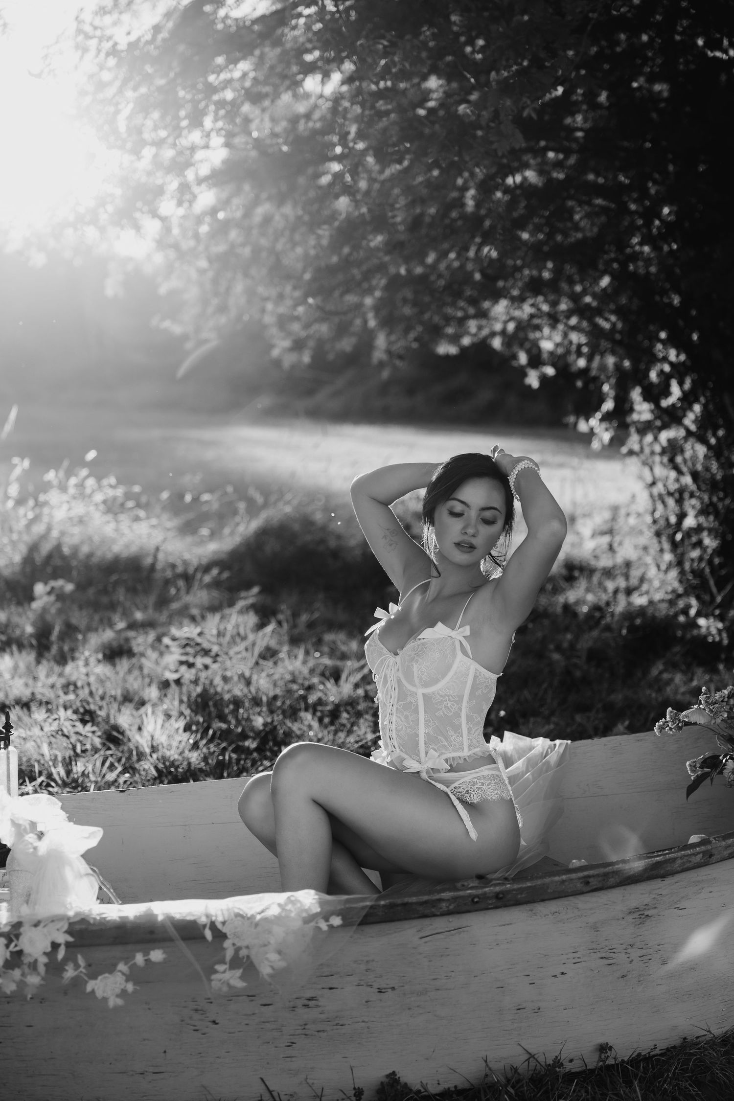 Black and white artistic photo of a woman in a white corset sitting in a vintage bathtub outdoors.
