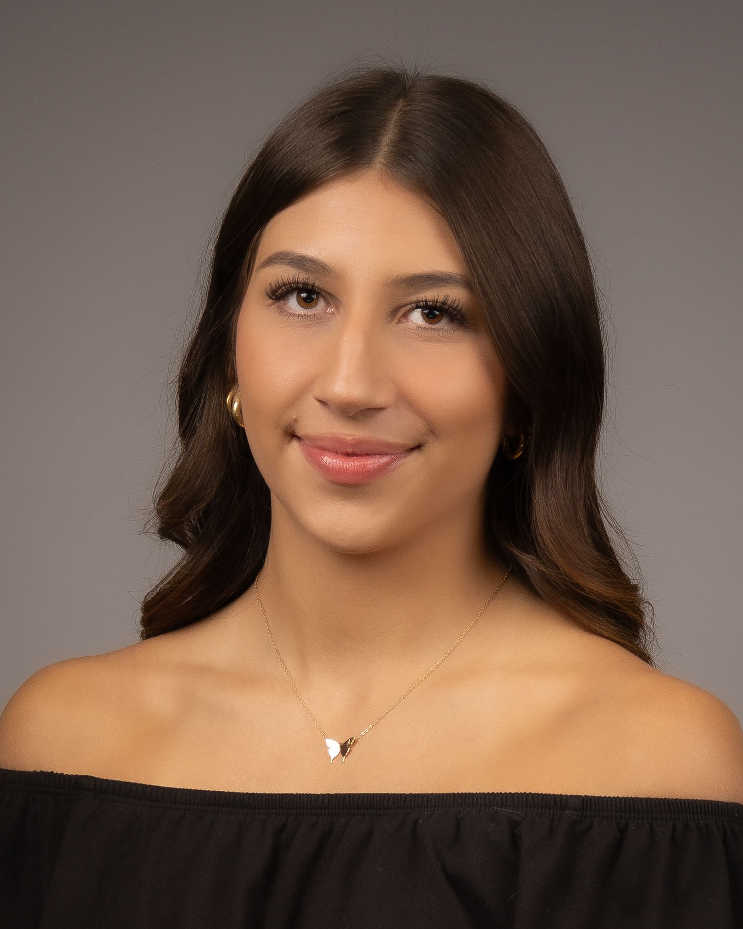 Studio portrait against grey background with off-shoulder top and delicate necklace.