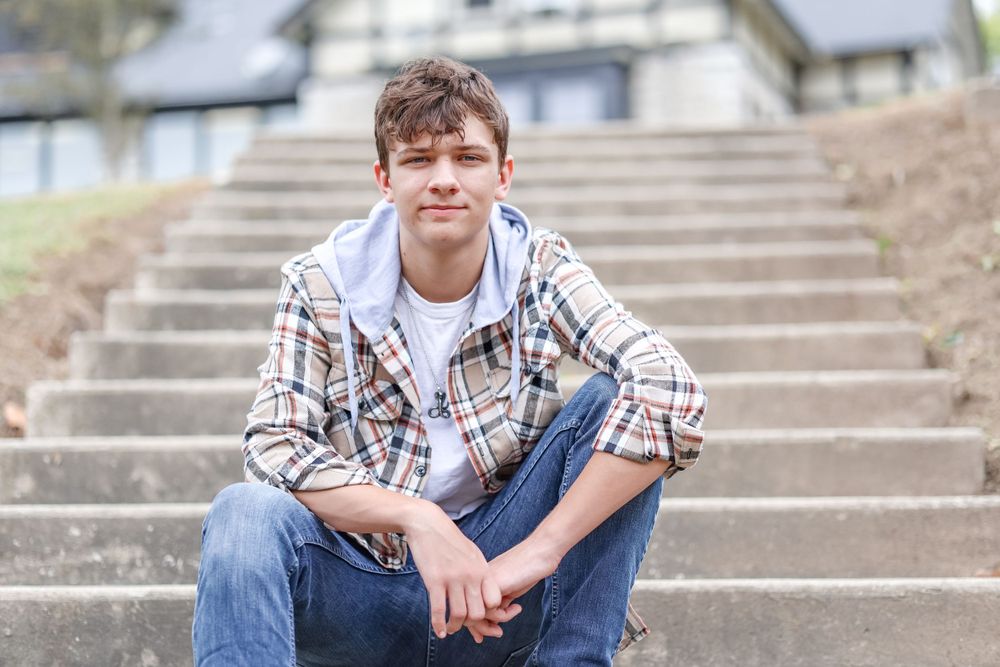 Senior with tan plaid shirt sits leisurely on steps with elbows naturally resting on knees