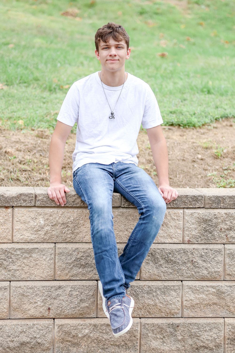 Senior in white shirt sits on brick wall