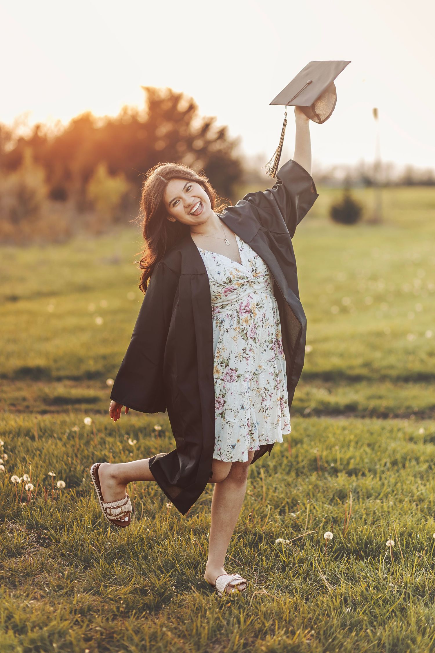Graduate in blue cap and gown smiling outdoors on campus.