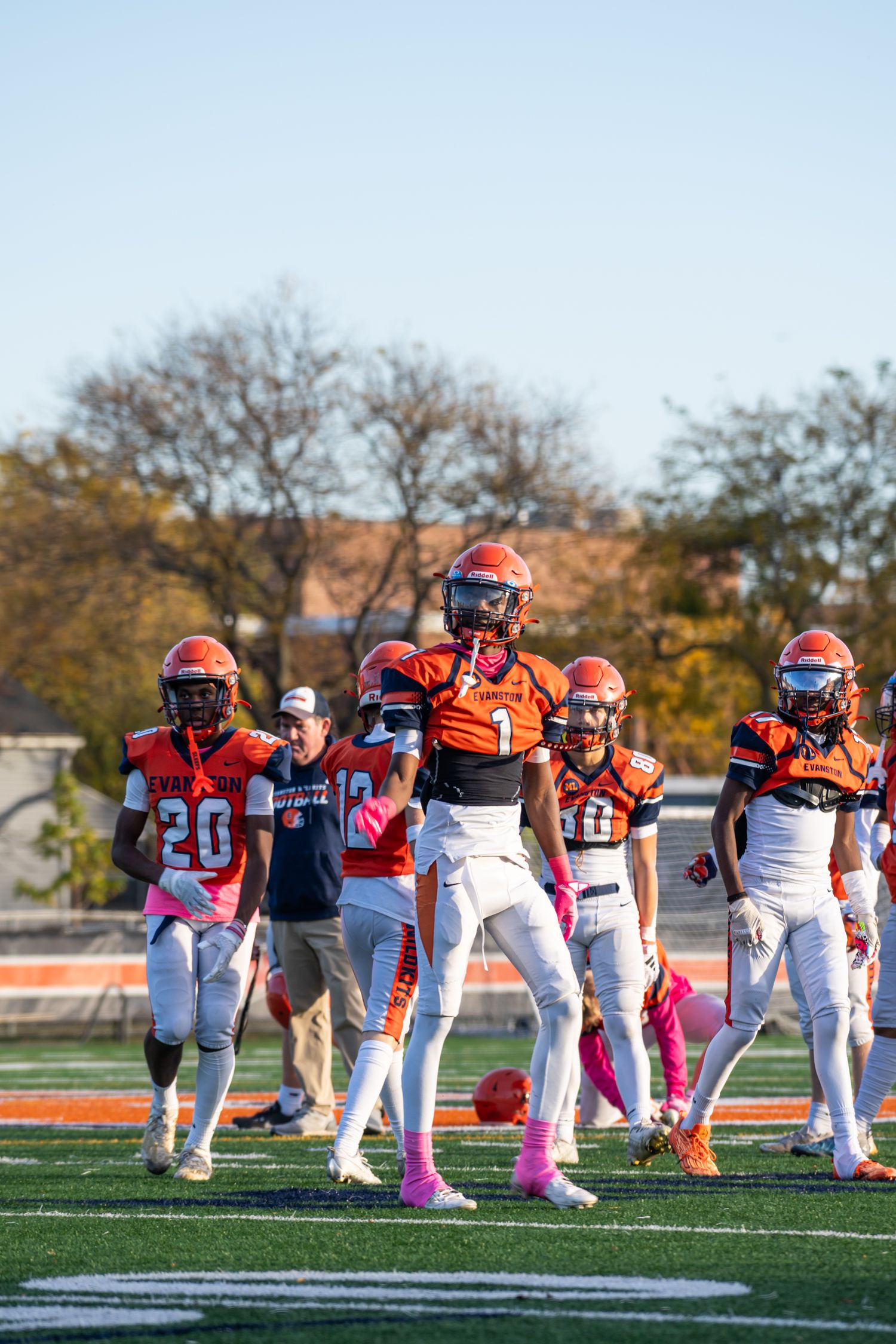 Football team in orange and white uniforms warming up on field during daytime.
