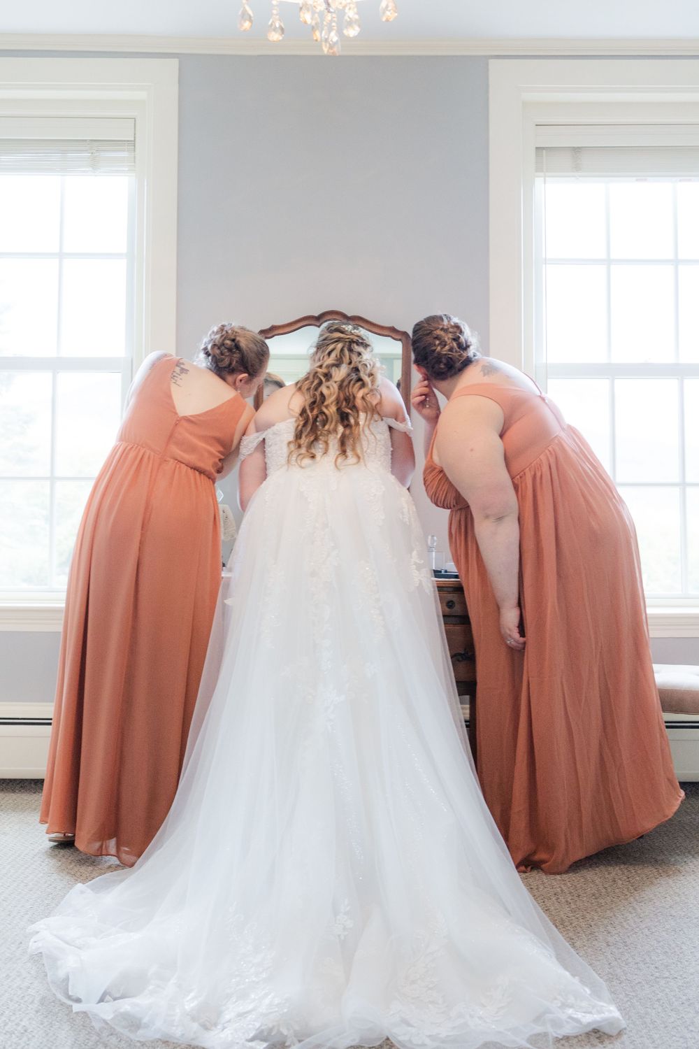 Two bridesmaids in peach dresses helping with wedding dress from behind.