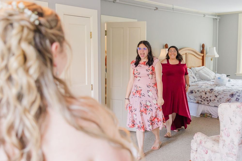 Wedding preparation scene with floral and burgundy dresses visible in mirror reflection.