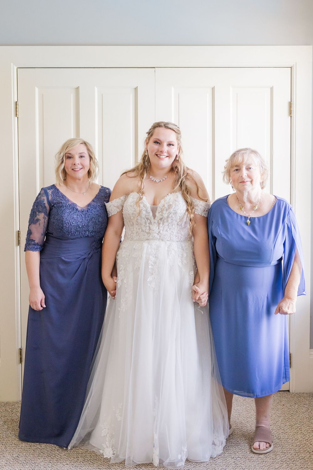 Three generations pose together in formal blue dresses and white wedding gown.