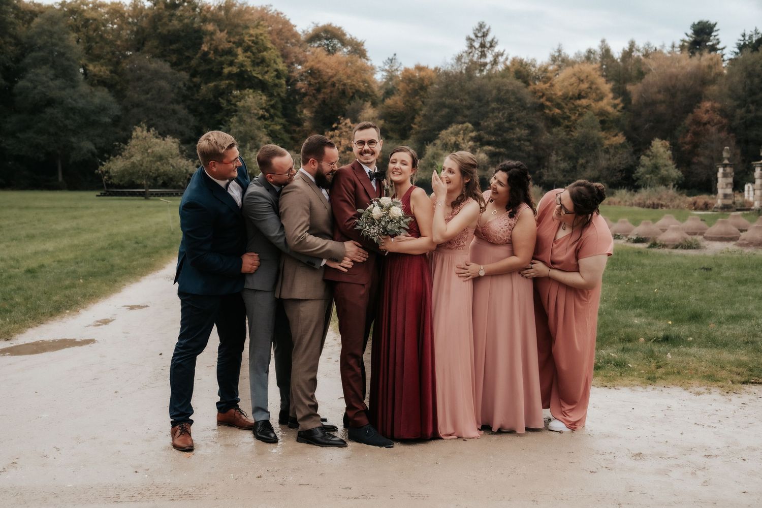 Wedding party in burgundy and pink dresses poses together on garden path.