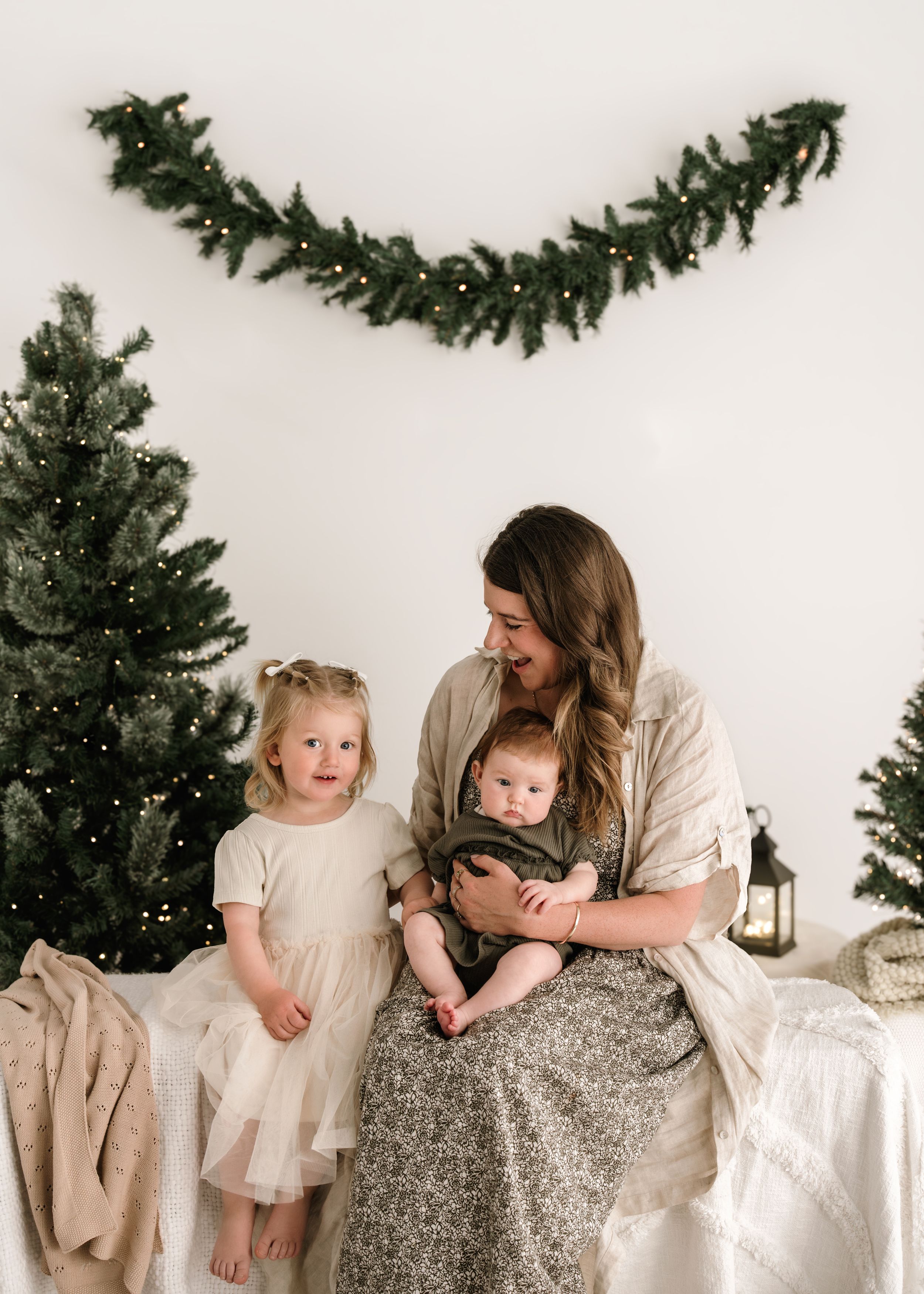 Family sits together on white floor with Christmas trees and lanterns creating a cozy holiday atmosphere.