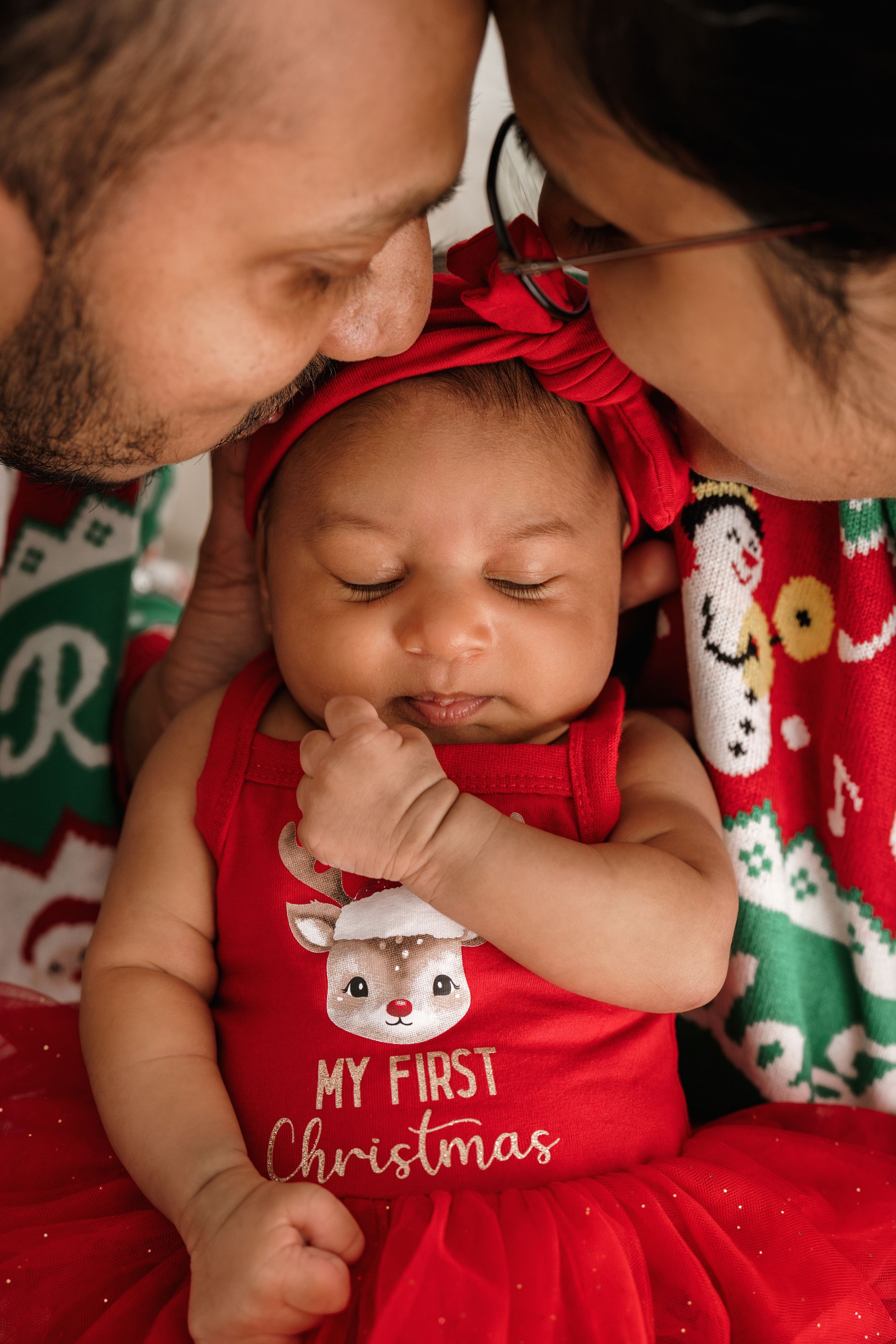 Baby in red 'My First Christmas' outfit sleeps peacefully on festive holiday blanket.